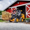 JCB 300 Skid Steer Loader hauling hay bales on a farm