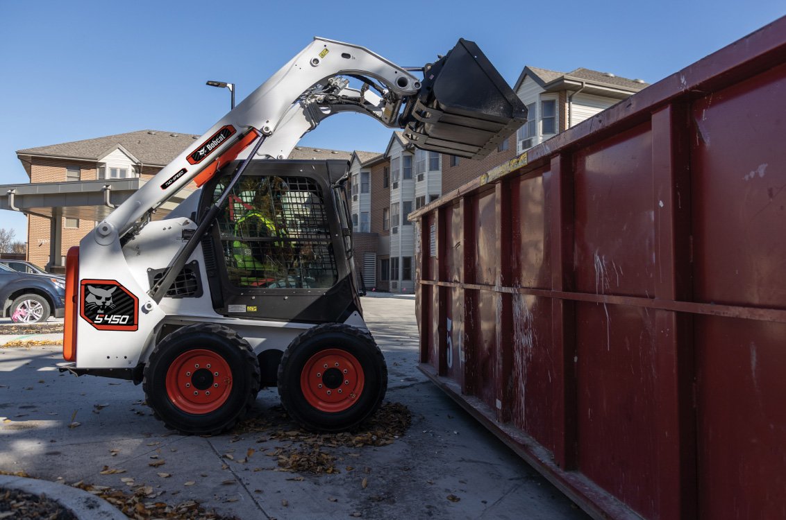 Bobcat S450 Skid Steer Loader dumping scrap into a container