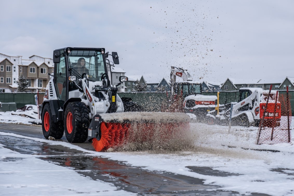 Bobcat L95 Compact Wheel Loader sweeping snow & dirt off a street